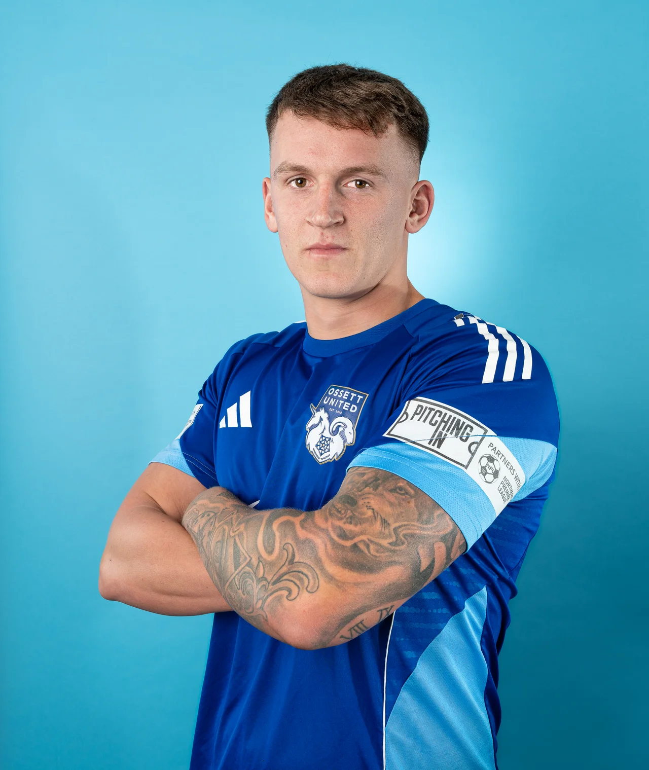 Player portrait in a blue sports shirt with folded arms.